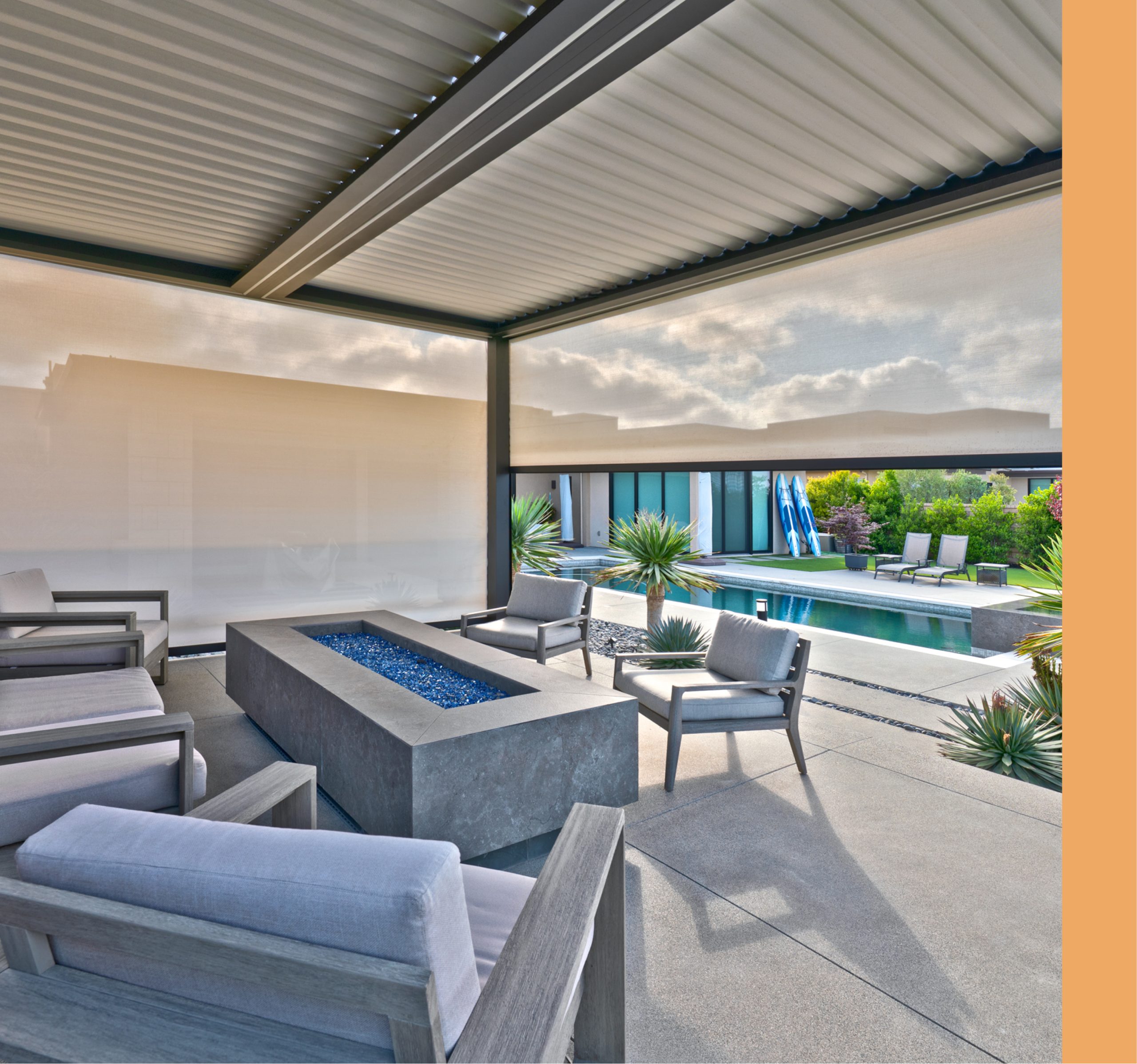 Louvered patio cover with a side sun screen shading an outdoor lounge and fire pit beside a backyard pool