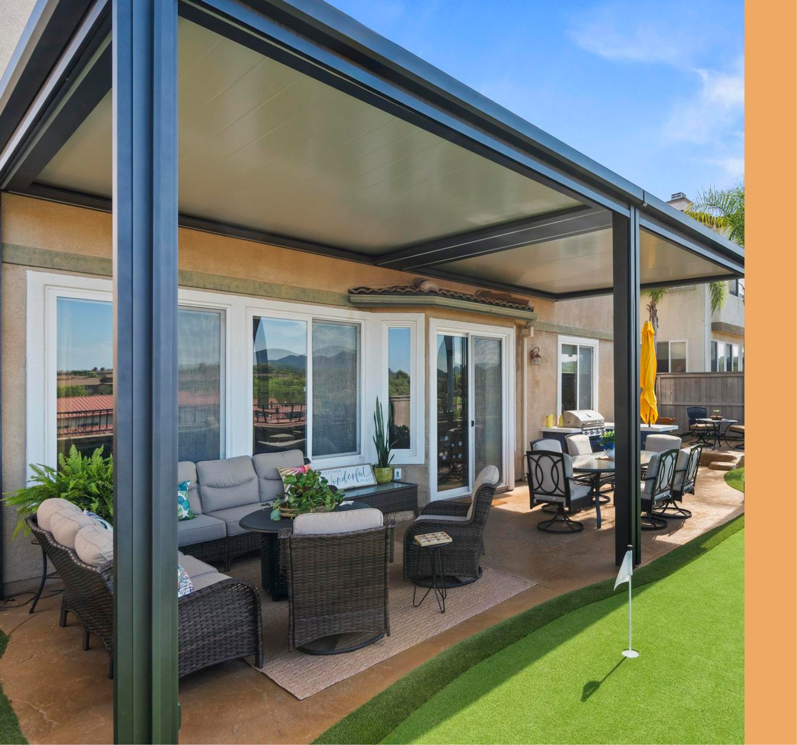 Dark-framed aluminum patio cover over an outdoor seating and dining area beside a backyard putting green.